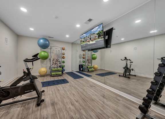 A home gym with a variety of exercise equipment including a stationary bike, a treadmill, and a television mounted on the wall. at Sunscape Apartments, Virginia