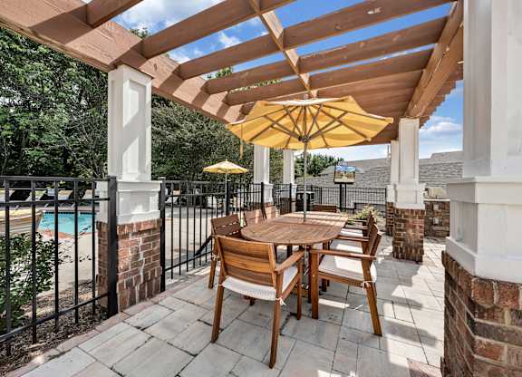 A wooden table and chairs are set up on a patio with a yellow umbrella. at Sunscape Apartments, Roanoke, Virginia