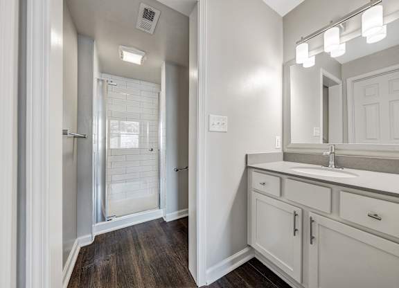 A bathroom with a sink, mirror, and a shower with a glass door. at Sunscape Apartments, Virginia