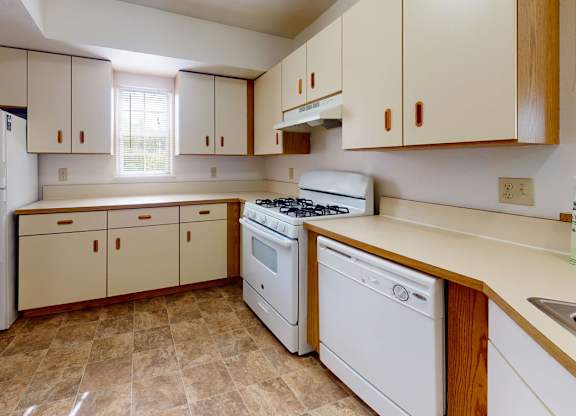A kitchen with a window, white appliances and wooden cabinets at Tall Oaks Apartment Homes, Michigan, 49009