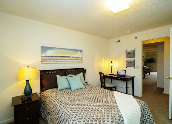 A bedroom with a bed, desk, and plush carpeting at Tall Oaks Apartment Homes, Michigan