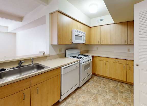 A kitchen with wooden cabinets and a white microwave, dishwasher, and gas stove at Tall Oaks Apartment Homes, Michigan