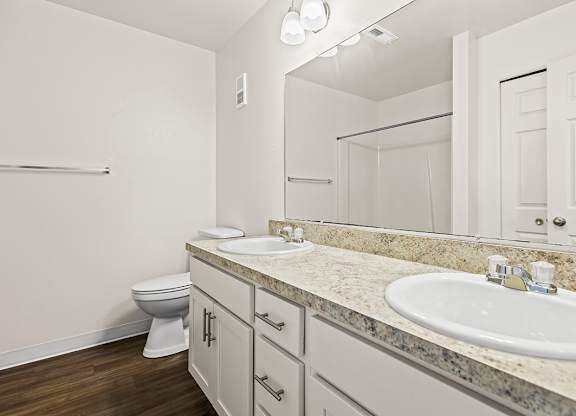 A bathroom with a toilet, two sinks, and mirror at Tanglewood Apartments, Oak Creek, WI