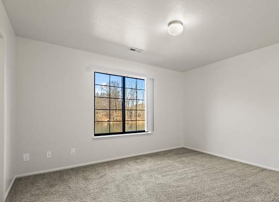 A spacious bedroom with a window and a carpeted floor at Tanglewood Apartments, Oak Creek, WI