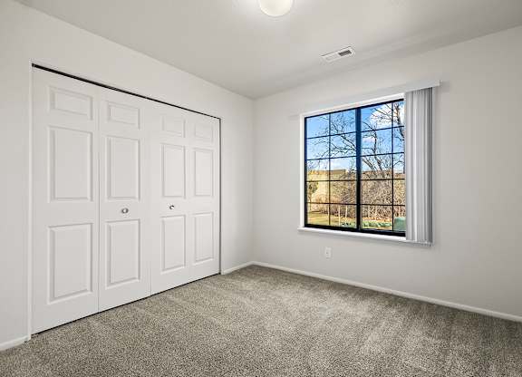 A bedroom with a large window and a white closet at Tanglewood Apartments, Oak Creek, WI