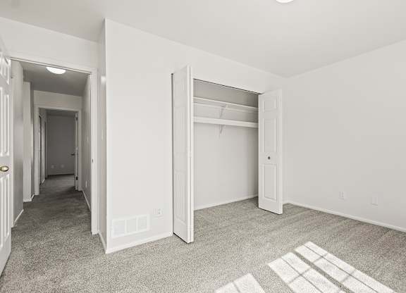 A bedroom with a carpeted floor and a white closet at Tanglewood Apartments, Oak Creek, WI