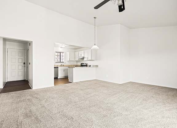 A large, empty dining and living room with a carpeted floor and a kitchen area in the background at Tanglewood Apartments, Oak Creek, WI