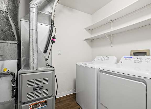 A washing machine is in a laundry room with a dryer and shelves at Tanglewood Apartments, Oak Creek, WI