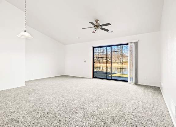 A spacious living room with a high ceiling, ceiling fan and a sliding glass door leading to a patio at Tanglewood Apartments, Oak Creek, WI