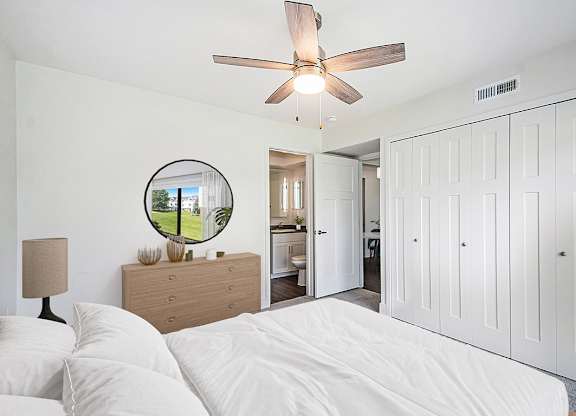 A bedroom with a bed, dresser, mirror, ensuite bath and a ceiling fan at The Crossings Apartments in Grand Rapids, MI