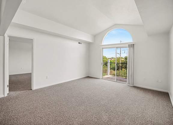 A large empty living room with a cathedral ceiling and a large arched window at Tracy Creek Apartments, Ohio