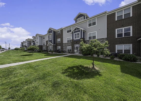 a green lawn with shade trees in front of an apartment building at Trade Winds Apartment Homes in Elkhorn, NE 68022