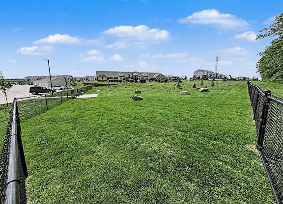 A large grassy dog park with a fence and buildings in the distance at Trade Winds Apartment Homes, Elkhorn, NE, 68022