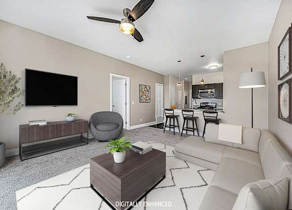 A living room with a grey armchair, a white sofa, a wooden coffee table, and a ceiling fan at Trade Winds Apartment Homes, Elkhorn, Nebraska