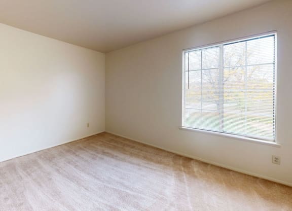 bedroom with a large window and plush carpeting  at Trappers Cove Apartments, Lansing, MI