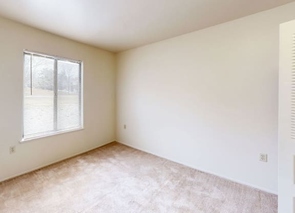 a bedroom with a window and a carpeted floor  at Trappers Cove Apartments, Lansing, 48910