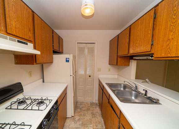 A kitchen with a gas stove and wooden cabinets at Trappers Cove Apartments, Lansing