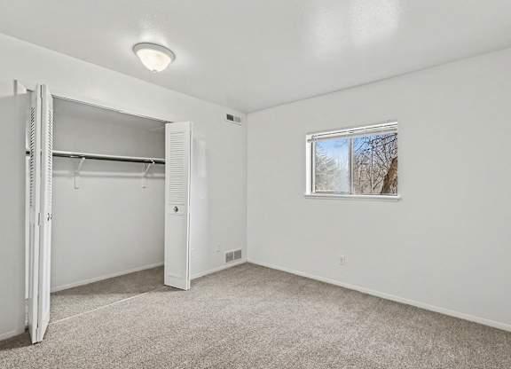 A white bedroom with a window and a white closet at Trappers Cove Apartments, Lansing
