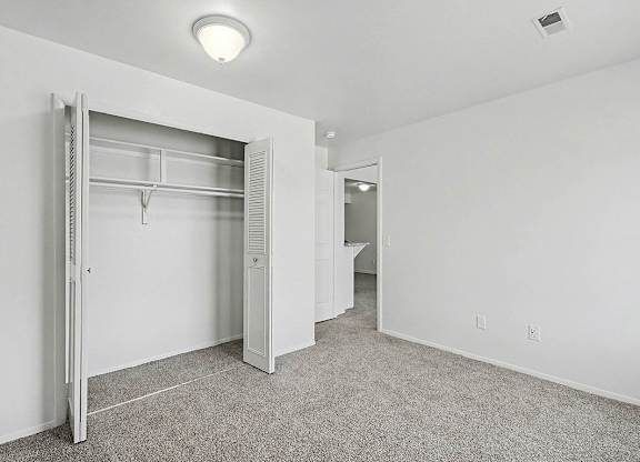 A white bedroom with a large closet and carpet at Trappers Cove Apartments, Lansing
