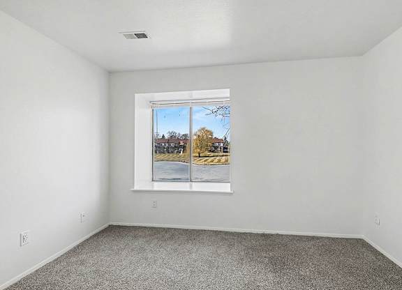 A bedroom with a large window showing a view of a pond at Trappers Cove Apartments, Lansing