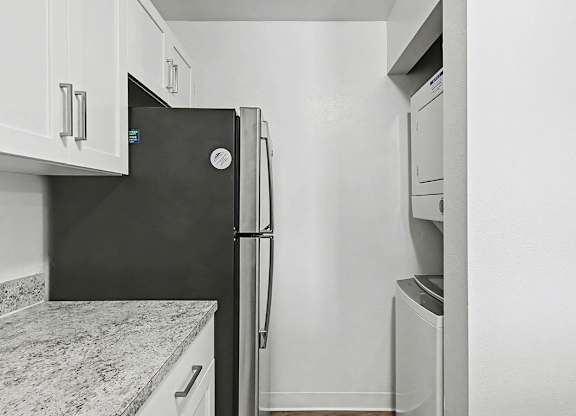 A stainless steel refrigerator in a kitchen with a washer and dryer at Trappers Cove Apartments, Lansing