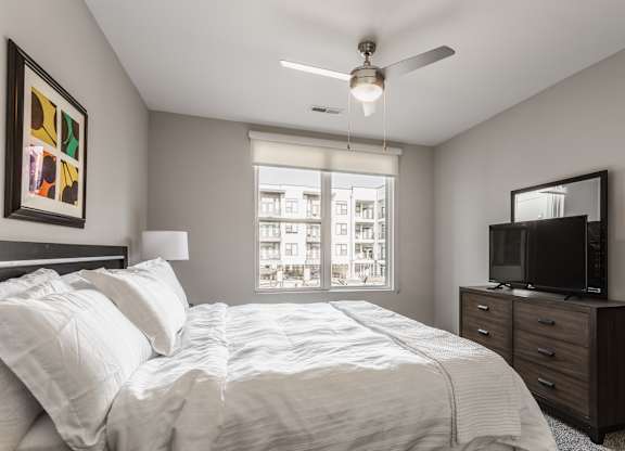 A bedroom with a large bed, a television, and a window overlooking a cityscape.