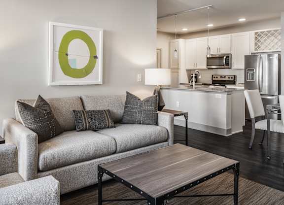 A modern living room with a grey couch, a coffee table, and a kitchen in the background.