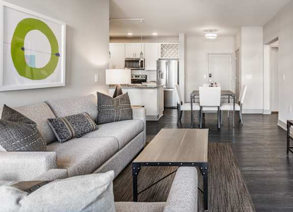 A modern living room with a grey couch, a wooden coffee table, and a large painting on the wall.