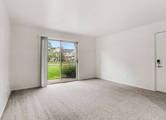 A living room with a carpeted floor and a sliding glass door leading to a patio and green lawn at Walnut Trail Apartments, Michigan