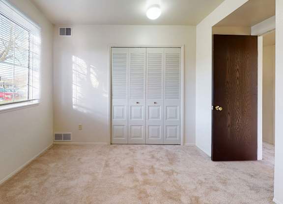 A bedroom with a closet door and a window with blinds at Walnut Trail Apartments, Michigan