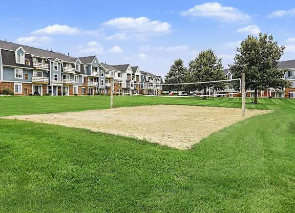 A volleyball net is set up on a sandy patch in the middle of a grassy area at Walnut Trail Apartments, Portage, MI