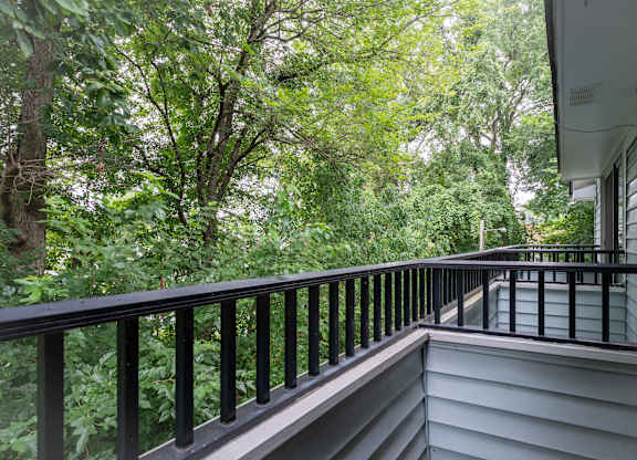 A balcony with a black railing overlooks a lush green forest at WaterFront Apartments, Virginia Beach, 23453