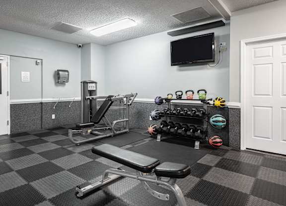A gym with a bench, weights, and a television at WaterFront Apartments, Virginia Beach, 23453