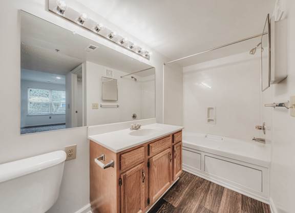 A white bathroom with a wooden vanity and a white bathtub at WaterFront Apartments, Virginia Beach, 23453