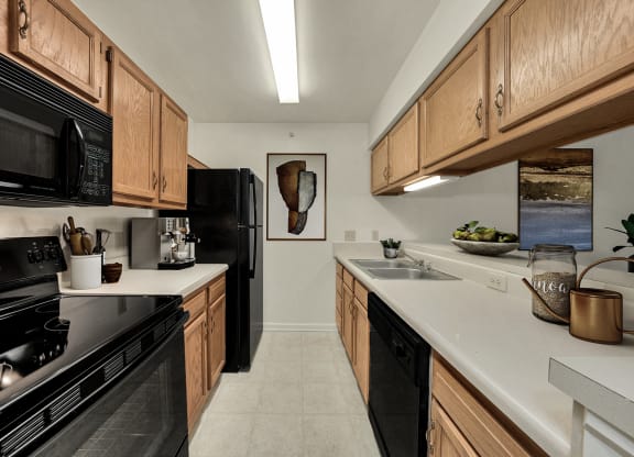 a kitchen with wood cabinets and black appliances and white counter tops at WaterFront Apartments, Virginia Beach, VA