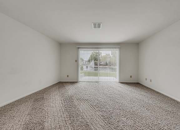 A room with a carpeted floor and a view of a fence and trees outside through a sliding glass door at WaterFront Apartments, Virginia Beach, 23453