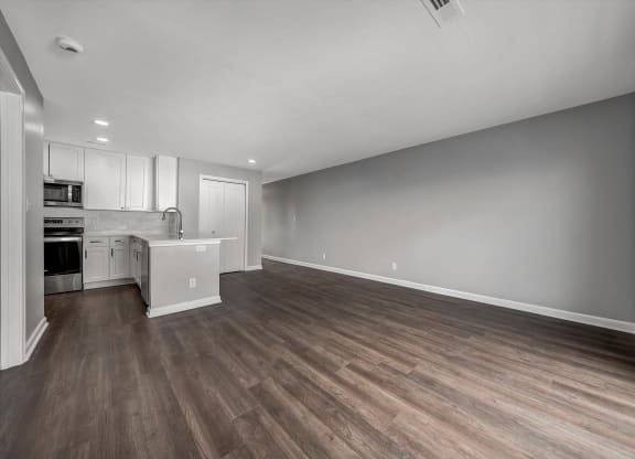 the living room and kitchen of an apartment with wood flooring and white cabinets at WaterFront Apartments, Virginia