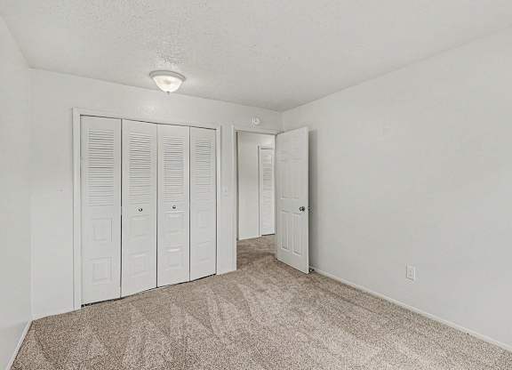 A bedroom with white walls and a carpeted floor with a large white closet at Waverly Park Apartments, Lansing