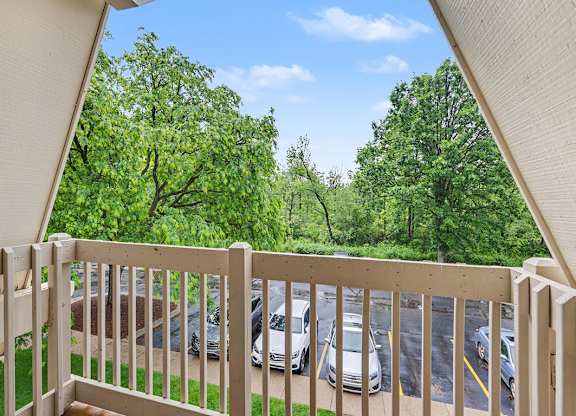 A balcony with a view of a parking lot and trees at Waverly Park Apartments, Lansing