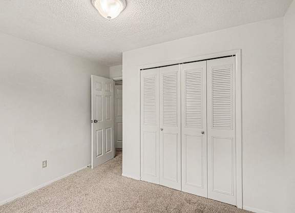 A white bedroom with a carpeted floor and a white door to a closet at Waverly Park Apartments, Lansing