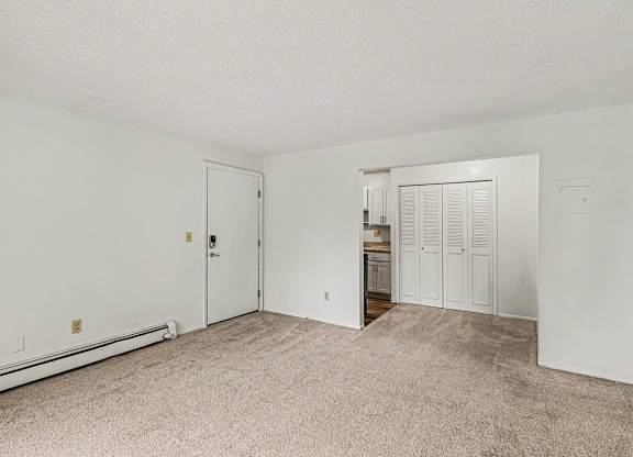 An entry door, a white living and dining room with a carpeted floor at Waverly Park Apartments, Lansing