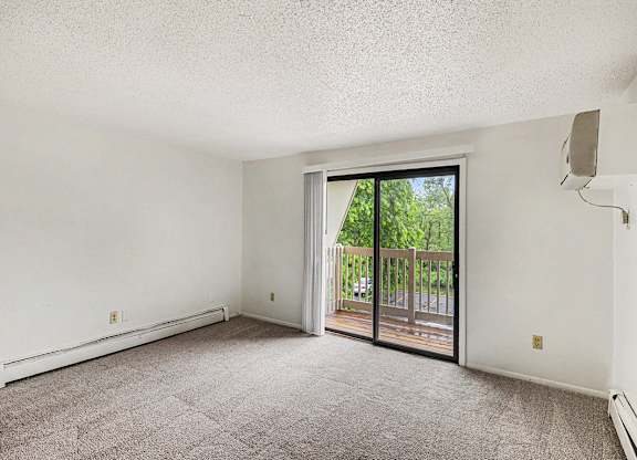 A living room with a carpeted floor and a sliding glass door leading to a balcony at Waverly Park Apartments, Lansing