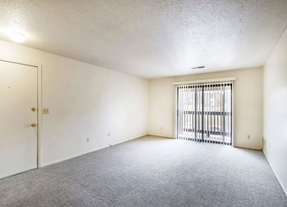 large living room with a sliding glass door to a balcony at West Wind Apartments in Fort Wayne, IN