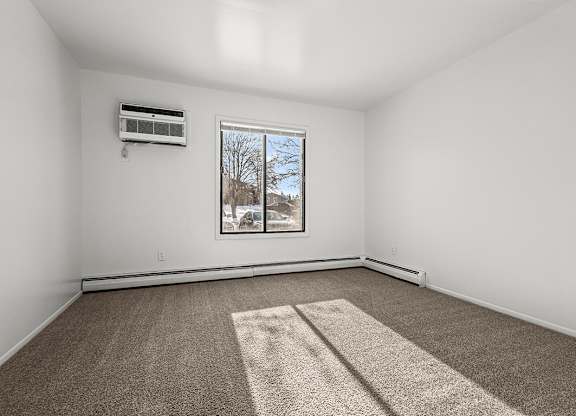 A spacious bedroom with a carpet, a window, and an air conditioner at Wood Creek Apartments, Kenosha