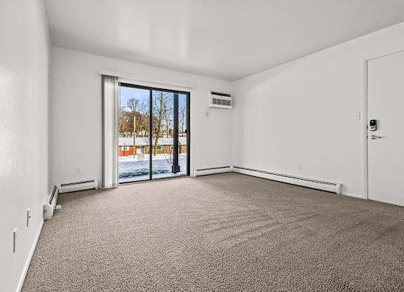 A living room with a carpeted floor and a sliding glass door leading to a patio at Wood Creek Apartments, Kenosha
