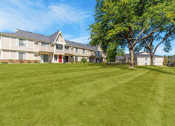 A large grassy field behind a building with a tree in the foreground at Wood Creek Apartments, Wisconsin