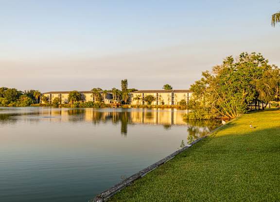 A serene lake with a building in the background and a tree on the right.