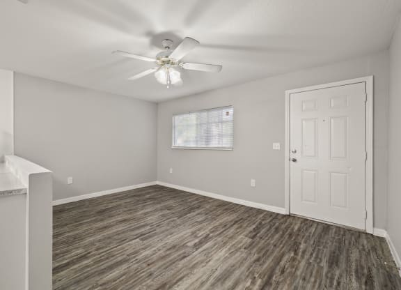 an empty living room with a white door and a ceiling fan