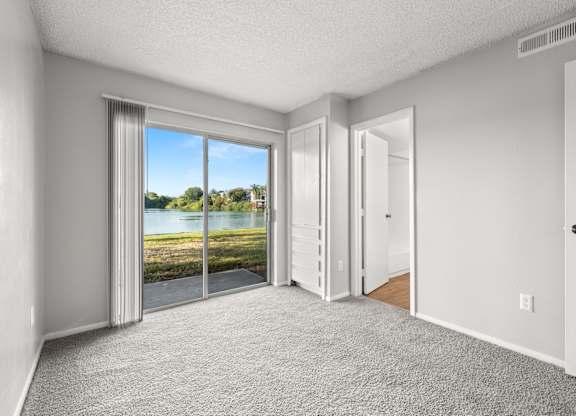 A room with a carpeted floor and a sliding glass door leading to a view of a lake.