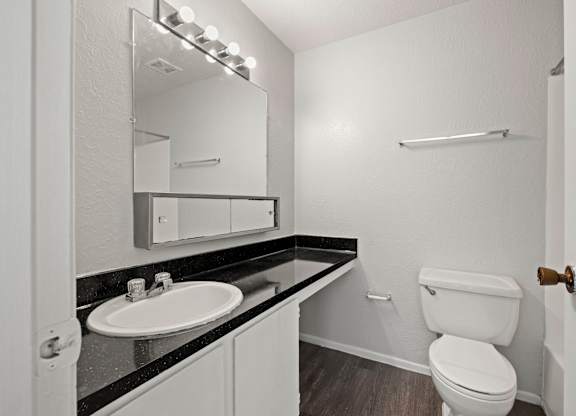 A bathroom with a toilet, sink, mirror, and lighting fixture.